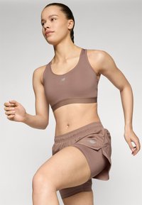 Ensemble de sport marron comprenant un soutien-gorge et un short, fabriqué en tissu extensible, avec un accent logo et une coupe décontractée pour le mouvement et le confort.