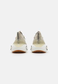 Beige and white athletic shoes with a mesh upper, rubber sole, and black accents. Features a translucent heel and textured sole.