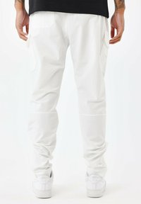 Pantalones cargo blancos hechos de una tela duradera, con bolsillos laterales, un ajuste entallado y puños elásticos, combinados con zapatillas blancas.