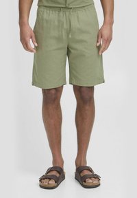Grønne linnedshorts med elastisk talje og snor, med oprullede kanter og sidelommer. Båret med brune sandaler.