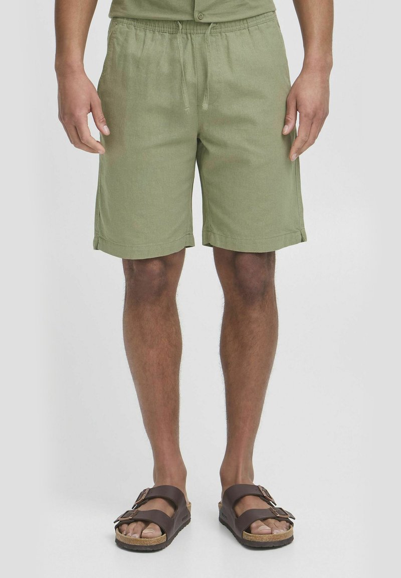 Grønne linnedshorts med elastisk talje og snor, med oprullede kanter og sidelommer. Båret med brune sandaler.