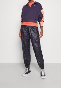 Felpa con zip navy e corallo con orlo elastico; pantaloni jogger a righe nere e viola; sneakers alte nere; dettagli con logo Nike.