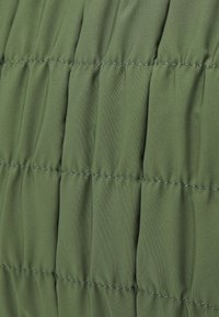 Grön kviltad tyg med vertikal sömnad, med en slät textur. Materialet verkar lätt och isolerat.