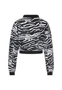 Chaqueta recortada en blanco y negro con un patrón de rayas de tigre, de mangas largas y con un cuello y puños de canalé negros. Textura de tejido suave.