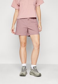 Ljusrosa t-shirt med ficka och snörning i nederkant, tillsammans med mauve shorts. Bärs med grå vandringsskor och vita ankelstrumpor.