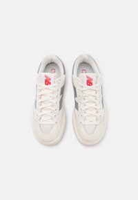 Vita och grå sneakers med ett nätöverdrag, texturerade överlägg och snörning. Röd logotyp på tungan och minimala detaljer. Rund tådesign.