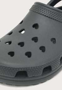 Gros plan d’une chaussure sabot grise avec des trous de ventilation en forme de cœur et des bords texturés pour l’adhérence et le confort.