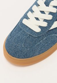 Jeans teniske z teksturiranim modrim zgornjim delom, belimi vezalkami in gumijastim podplatom s zaobljenim nosom ter šivanjem.