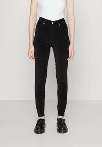 Svarta kordflortbyxor med hög midja och smal passform, med framfickor och detaljer i metallknappar, tillsammans med svarta snörskor.