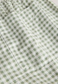 Közeli kép világoszöld és fehér kockás anyagról, rávarrt zsebbel, részletes varrással.