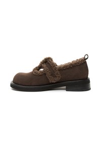 Scarpa Mary Jane in suede marrone con rifiniture in peluche, punta tonda, suola bassa nera e chiusura con strap regolabile, vista laterale su sfondo bianco.