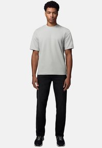 Lys grå kortærmet t-shirt, afslappet pasform, parret med sorte jeans. Modellen bærer sorte sneakers og står mod en ensfarvet baggrund.