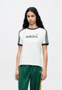 White cotton t-shirt with black collar and cuffs, featuring "adidas" logo in black. Paired with green track pants with yellow stripes.
