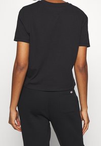T-shirt nera in cotone a maniche corte con scollatura rotonda, design cropped e maniche orlate. Presenta un piccolo logo vicino al fondo.