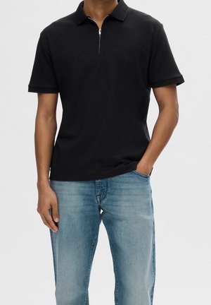 Black polo shirt with a zippered collar, short sleeves, and a slim fit. Paired with light blue jeans. Simple, modern design with clean lines.