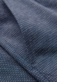 Close-up van gestructureerde blauwe stof met een fijn, herhaald geweven patroon dat over zichzelf is gevouwen.