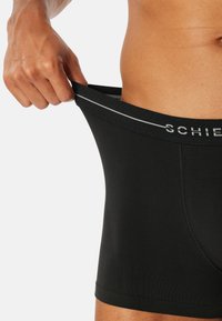 Boxer neri realizzati in tessuto liscio, con un'elastico grigio con marchio e un design aderente. Il tessuto sembra traspirante.