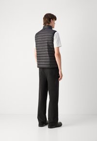 Schwarze gepolsterte Weste mit hohem Kragen, horizontalen Nähten und minimalistischem Design, kombiniert mit schwarzen Hosen und schwarzen Schuhen.
