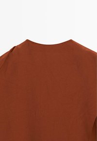 Rustfarvet top med rund halsudskæring, der har en glat tekstur og let rynkning. Minimalistisk design uden synligt hardware eller accenter.