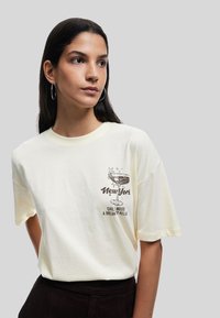Cremefarvet bomulds T-shirt med korte ærmer, der har et grafisk tryk af et cocktailglas samt teksten: "New York", "Chill Mood" og "A Break to Relax."