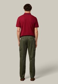 Rode poloshirt met kraag, gecombineerd met olijfgroene cargobroek met zijzakken. De outfit wordt afgerond met bruine schoenen.
