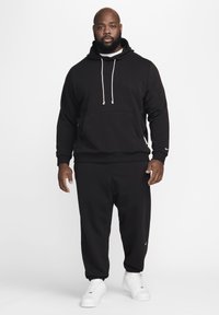 Felpa nera con cappuccio e coulisse, con tasca frontale, abbinata a pantaloni della tuta neri. Indossata con sneakers bianche. Design semplice, senza motivi.