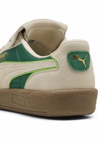 Beige ruskindsneakers med grønne syntetiske accenter, tekstureret gummisål og gyldent logodetalje på hælen. Velcro-strap til lukning.