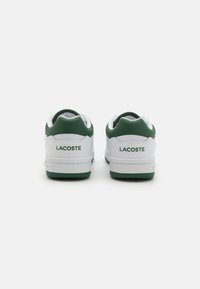 Baltos sportbačiai su žaliais akcentais. Lygaus odos viršus, raišteliai, ir guminis padas. Žalias "LACOSTE" logotipas spausdintas ant nugaros.