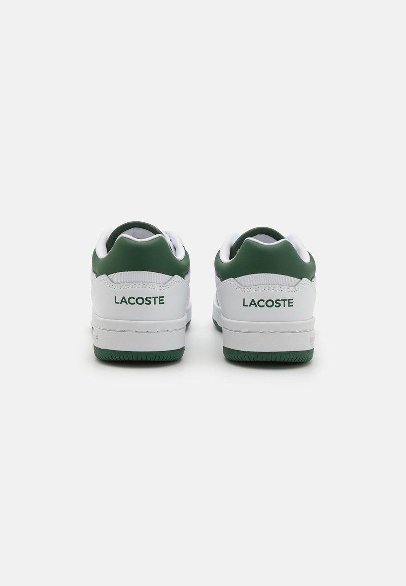 Witte sneakers met groene accenten. Gladde leren bovenkant, vetersluiting en rubberen zool. "LACOSTE" logo in het groen gedrukt op de achterkant.