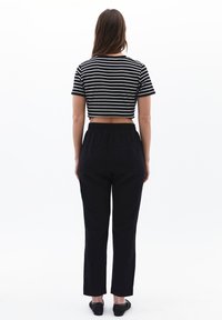 Schwarze hoch taillierte Hosen mit elastischem Bund, kombiniert mit einem schwarz-weiß gestreiften Crop-Top, von hinten betrachtet, glatte Textur.