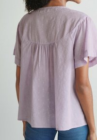 Lavendel kortærmet bluse med teksturerede prikker, samlet rygdesign og afslappet pasform, lavet af letvægtsstof.