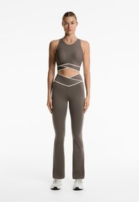 Braunes Sport-Outfit mit einem kurzärmeligen, ärmellosen Oberteil mit weißen Akzenten. Eng anliegende Hose mit weit ausgestellten Beinen. Glatte Textur, minimalistisches Design.