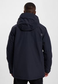 Tamsiai mėlynas paminkštintas švarkas su dideliu gobtuvu, užtrauktuku ir logotipu ant peties. Pagamintas iš lygios, vandeniui atsparios medžiagos.