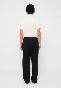 Camisa polo de manga curta branca e calças de treino pretas, com um cós elástico e um bolso traseiro, com uma textura de algodão suave.