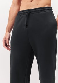 Black sweatpants with a textured waistband, adjustable drawstring, and side pockets. Made of soft fabric with a relaxed fit.