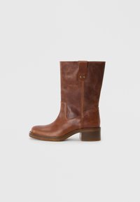 Botte en cuir marron, haut jusqu'au genou, avec un bout arrondi, un panneau latéral contrastant et un petit talon carré. Comprend une languette à l'arrière et des clous en métal.
