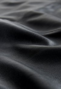 Schwarzes Ledergewebe mit glatter Textur, das weiche Drapierungen und dezenten Glanz aufweist und natürliche Falten sowie Narbenmuster zeigt.