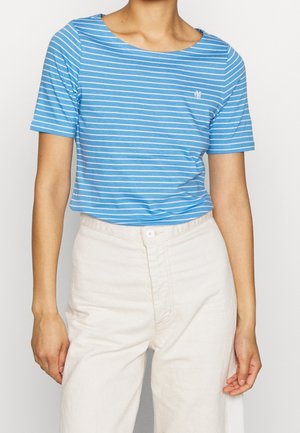 Personne portant une chemise à rayures bleues et blanches à manches courtes, rentrée dans un pantalon taille haute off-white avec un bouton à l'avant.