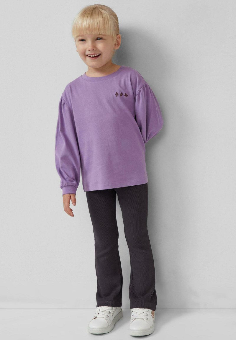 Paarse lange mouwen shirt met pofmouwen en bloemige borduursels; gecombineerd met donkergrijze broek en witte sneakers. Soepele stofstructuur.