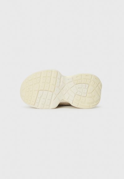 Sohle eines beigen Sneakers mit strukturiertem, quadratischem Profil auf einem schlichten weißen Hintergrund.