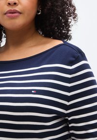 Μπλε ναυτικό και λευκή μακρυμάνικη μπλούζα με σχεδιασμό χωρίς ώμους. Διαθέτει ένα μικρό λογότυπο κεντημένο στο στήθος. Κατασκευασμένη από μαλακό ύφασμα.