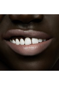 Nærbilde av lepper med en matt rosa leppestift, jevn tekstur og lyse hvite tenner mot mørk hud.