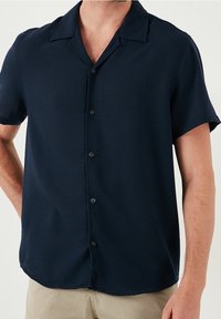 Ciemnogranatowa koszula z krótkim rękawem wykonana z gładkiej tkaniny, z kołnierzem z wycięciem i sześcioma guzikami z przodu. Subtelna faktura, czyste linie.