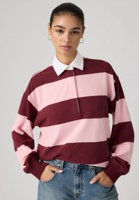 Μακρυμάνικο πόλο με μπορντό και ροζ ριγέ, με λευκό γιακά, εμπρόσθιο κουμπωτό και ριμπ μανσέτες. Κανονική εφαρμογή με χαλαρούς ώμους.