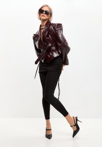 Blazer in ecopelle bordeaux con maniche a sbuffo e vita cintrata, abbinato a una gonna nera arricciata e leggings, e tacchi a punta neri.