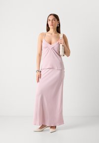 Lys pink kjole med tynde stropper, der har en indsnævret v-hals og lagdelt design. Styled med et lysfarvet bælte og beige spidse sko.