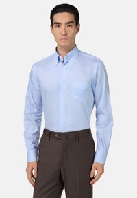 Jasnoniebieska koszula w paski z kołnierzykiem button-down, pojedynczą kieszenią na piersi i długimi rękawami. Skrojona do brązowych spodni, podkreślająca dopasowany krój.