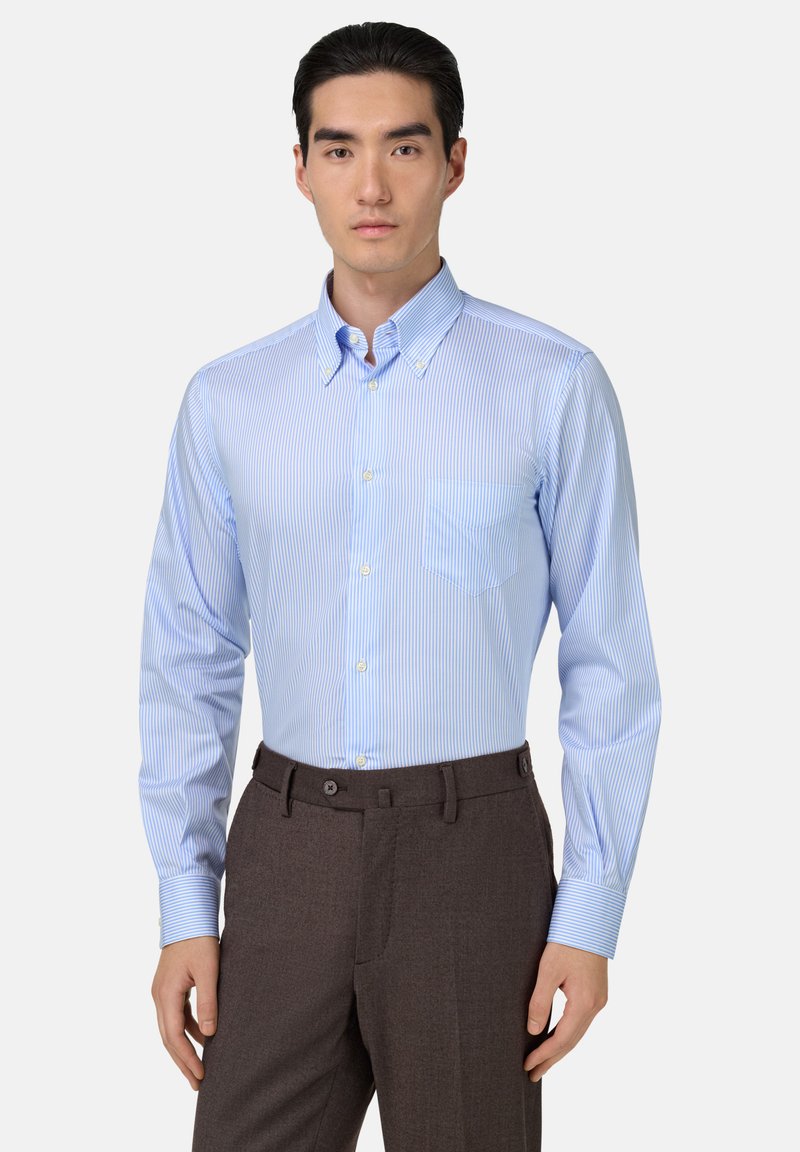 Jasnoniebieska koszula w paski z kołnierzykiem button-down, pojedynczą kieszenią na piersi i długimi rękawami. Skrojona do brązowych spodni, podkreślająca dopasowany krój.