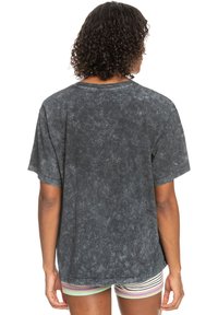 Camiseta negra con lavado ácido, de manga corta, con un cuello redondo, corte holgado y un acabado texturizado. Diseño minimalista sin patrones visibles.