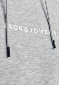 Szürke kapucnis pulóver, puha anyagból készült, elöl fehér "JACK&JONES" logóval, húzózsinórral és fekete fém végződésekkel.